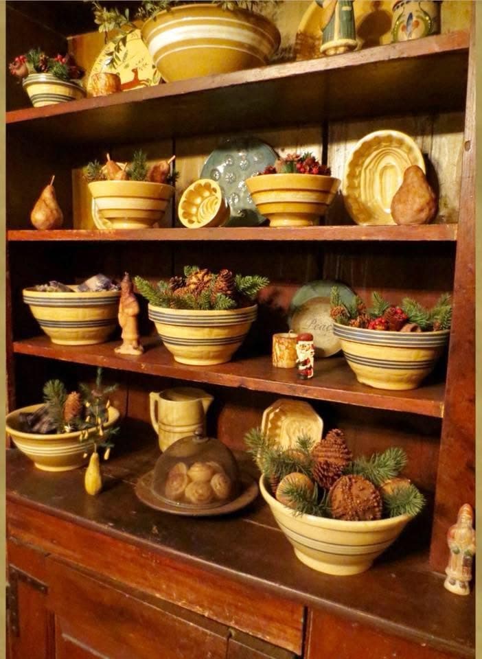 A deep walnut cupboard stacked with antique yellowware bowls and greenery